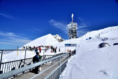 藍天雪景與山巔電信塔旁的遊客身影