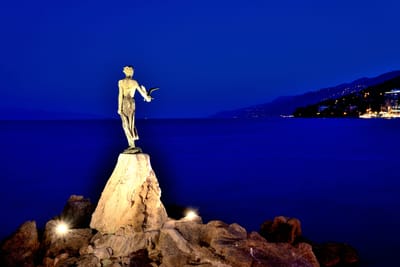 夜色中佇立海岸岩石上的少女與海鷗銅像